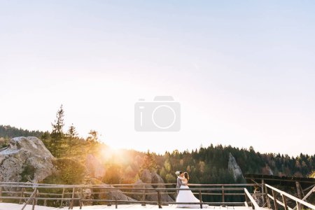 Foto de Beautiful couple of newlyweds, bride and groom in wedding dresses, walking against the backdrop of mountains - Imagen libre de derechos