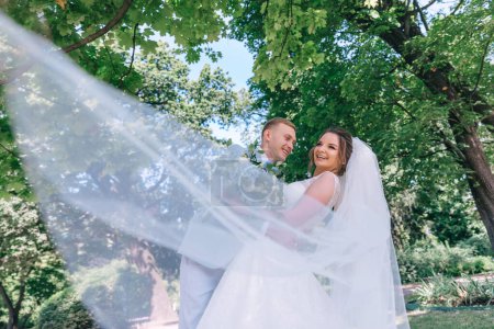 Téléchargez les photos : Élégants mariés posant ensemble dans la rue le jour de leur mariage sur fond de nature verte. - en image libre de droit