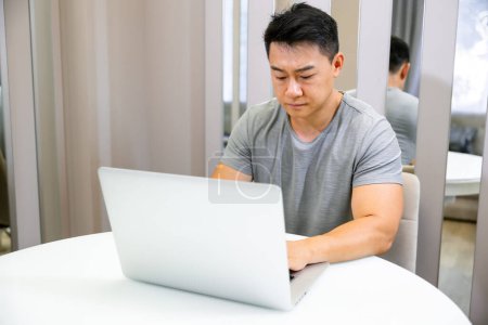 Foto de Hombre asiático trabajando en PC portátil en interiores en la sala de estar. Hombre cansado usando la computadora para el descanso, el estudio o la educación - Imagen libre de derechos
