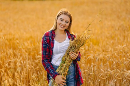 Photo for Attractive girl in red shirt with wheat smiles to camera in middle of wheat field - Royalty Free Image