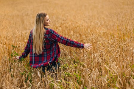 Photo for Blonde-haired woman in a red shirt posing in a wheat field, rear view - Royalty Free Image