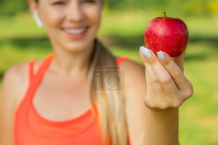 Photo for Cropped image of beautiful young sports lady smiling, holding an apple - Royalty Free Image
