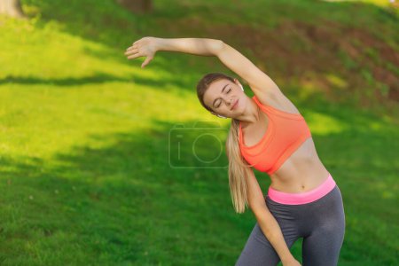 Photo for Young female workout before fitness training session at the park. She is stretching her arms and looking away,hi key. - Royalty Free Image