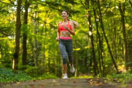 Téléchargez les photos : Femme heureuse courant dans le parc de la ville. Fille coureuse jogging souriant aspiration à l'extérieur sur belle journée d'été. - en image libre de droit