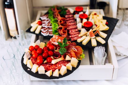 Foto de Deliciosa mesa con diferentes carnes, quesos y tomates en recepción de boda en restaurante. - Imagen libre de derechos