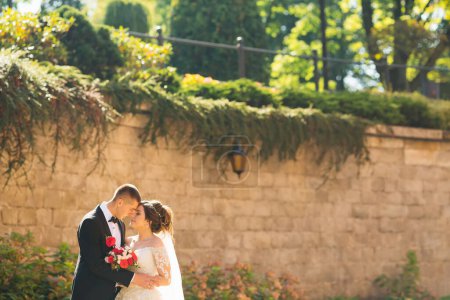Téléchargez les photos : Mariée et marié debout face à face et profiter du jour du mariage sur le fond du mur et les arbres. journée ensoleillée - en image libre de droit