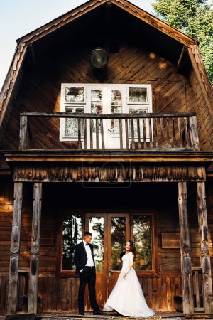 Foto de Pareja de bodas de pie en el porche de la construcción de madera. hermosa fachada antigua - Imagen libre de derechos