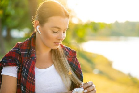 Téléchargez les photos : Gros plan de la femme utilise les véritables écouteurs sans fil blancs à la main pour mettre dans l'oreille et le contrôle - en image libre de droit