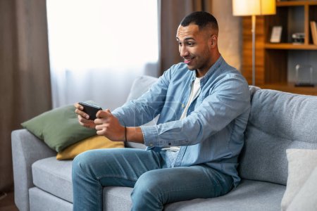Téléchargez les photos : Online gaming concept. Portrait of positive guy playing video games on smartphone at home on sofa - en image libre de droit