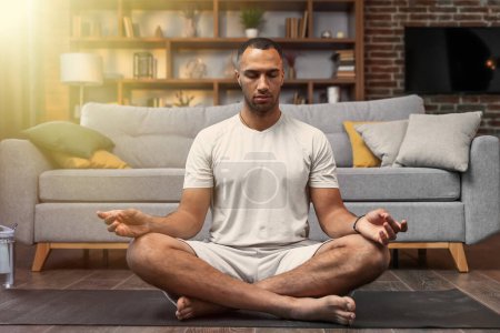 Téléchargez les photos : Meditation concept. Calm man meditating while sitting in lotus position relaxing doing yoga at home - en image libre de droit