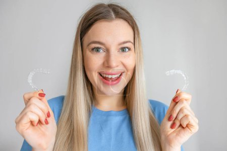 Foto de Cheerful woman holding transparent mouthguards for bite correction in clinic. A girl with a beautiful snow-white smile uses silicone braces - Imagen libre de derechos