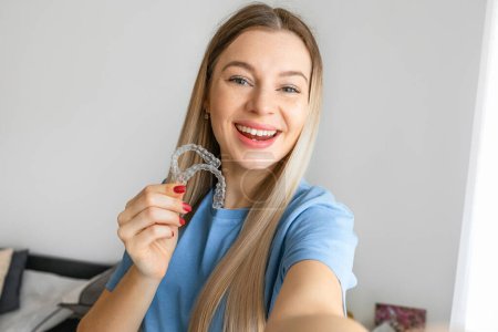 Téléchargez les photos : Femme médecin tenant un aligneur dentaire transparent et faire selfie, recommandant ce nouveau traitement. Concept de soins dentaires. - en image libre de droit