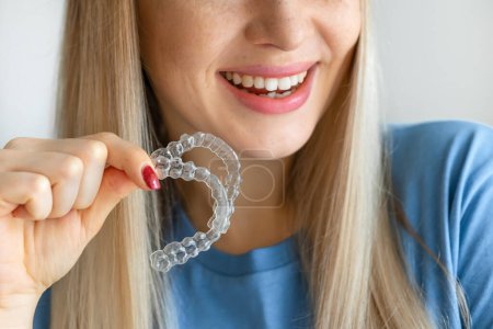 Zugeschnittenes Foto einer jungen schönen Frau mit lächelndem Händchen, das Zahnausrichterhalter hält (unsichtbar) auf weißem Hintergrund der Zahnklinik für schöne Zahnbehandlung Kurskonzept