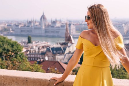 Téléchargez les photos : Une jeune femme blonde heureuse regarde les sites touristiques de Budapest, souriante, profitant du panorama - en image libre de droit