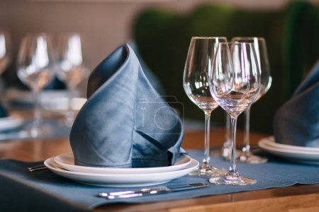 Téléchargez les photos : New white china dinner plates with gray napkins and empty wine glasses. Serving is waiting for guests at home or in a restaurant - en image libre de droit
