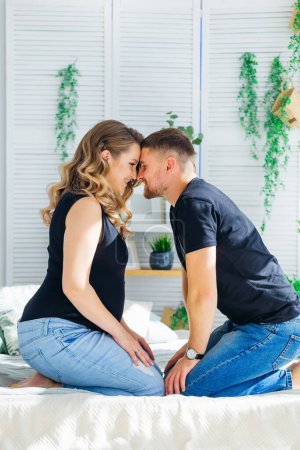 Photo for A happy family expecting a child. A pregnant woman sits with her husband in a cozy apartment, hugging her stomach - Royalty Free Image