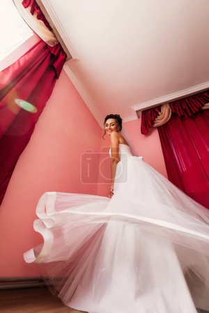 Téléchargez les photos : Mariée gaie dans une robe blanche dansant dans l'appartement avant la cérémonie. Matin de la mariée - en image libre de droit