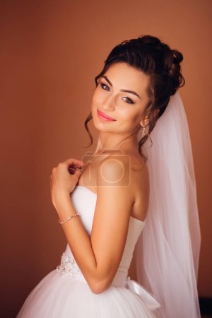 Foto de Una hermosa mujer joven en un vestido de novia blanco en el fondo del interior de un apartamento de lujo. Elegante y elegante mañana de la novia - Imagen libre de derechos