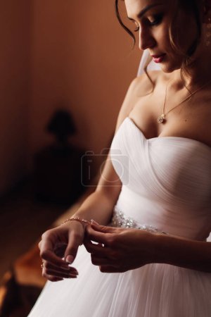 Téléchargez les photos : Préparation du matin pour le mariage. Rassemblement de la mariée. Une jeune femme en robe porte un bracelet en or avec des pierres sur la main avant la cérémonie - en image libre de droit
