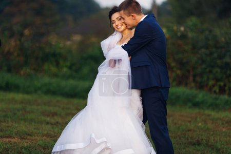 Téléchargez les photos : Un homme heureux serre doucement et fermement la mariée par derrière et l'embrasse le jour du mariage - en image libre de droit