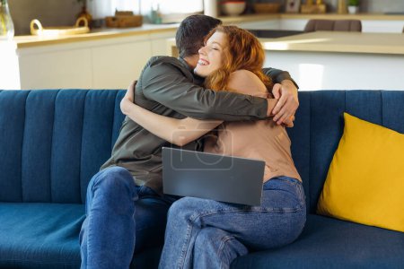 Foto de Smiling, happy and hugging couple enjoying, embracing and loving remote work together at home. Young romantic partners working online and celebrating successful news or job success letter on a sofa - Imagen libre de derechos