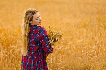 Téléchargez les photos : Jeune belle fille avec de longs cheveux blonds pose dans un champ de blé en été au coucher du soleil. Espace de copie - en image libre de droit