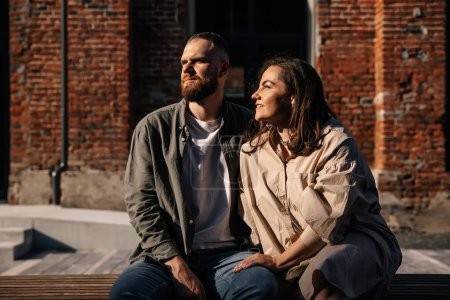 Photo for Attractive trendy dressed young couple sitting together on bench near brick wall. - Royalty Free Image