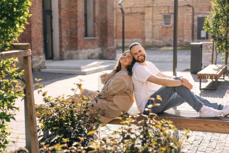 Téléchargez les photos : Couple joyeux ont assis sur le banc par temps ensoleillé dans le parc de la ville. - en image libre de droit