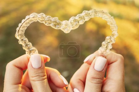 Foto de Mujer sosteniendo dos alineadores dentales transparentes en forma de corazón en la calle - Imagen libre de derechos