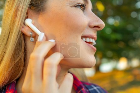 Photo for Close up of woman is using white true wireless earphones by hand to put in ear and control - Royalty Free Image