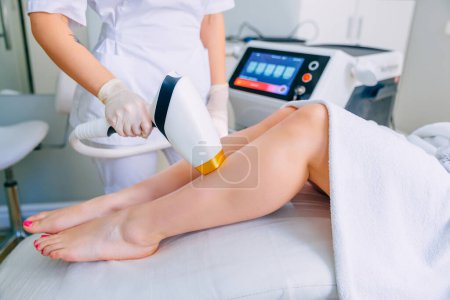 Photo for Beautician removes hair on beautiful female legs with a high-quality laser device. - Royalty Free Image