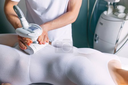 Foto de Una mujer recibe terapia cosmética contra la celulitis usando una máquina. masajista haciendo masaje corporal reafirmante - Imagen libre de derechos