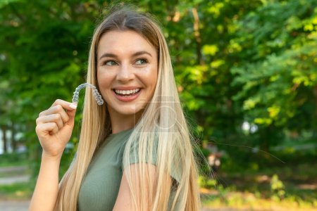 Beautiful smiling caucasian woman is holding invisaligner. Includes copy and text space.