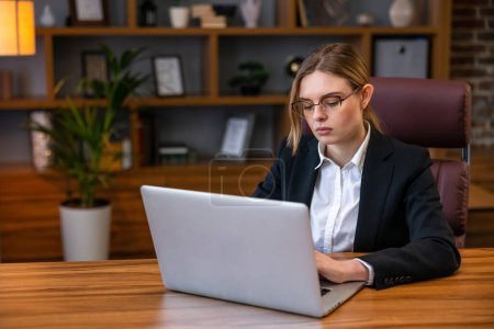 Foto de Joven mujer de negocios segura de trabajar en el escritorio de la oficina y escribir con un ordenador portátil, estantes en el fondo - Imagen libre de derechos