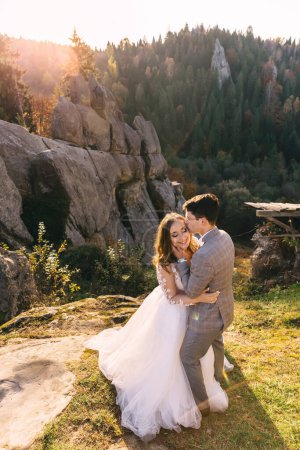 Photo for Stylish groom hugging happy bride in sunlight, romantic moment, boho wedding couple, luxury ceremony at mountains with amazing view - Royalty Free Image