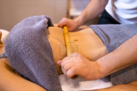 Téléchargez les photos : Gros plan de l'estomac d'une femme ayant une séance de massage anti-cellulite, thérapeute professionnel tenant des outils en bois en studio ou salon. - en image libre de droit