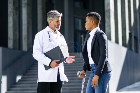 Photo for Senior male doctor and female patient talking about the diagnosis on the street, the man holds a folder with the results of the woman's tests - Royalty Free Image