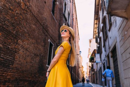 Photo for Stylish girls in a yellow dress and sunglasses looking at the building and smile. street, city, building - Royalty Free Image