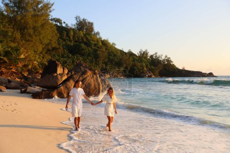 Foto de Hermosa pareja de amantes pasea por las Seychelles sobre el fondo de piedras, salpicaduras, cogidas de la mano - Imagen libre de derechos