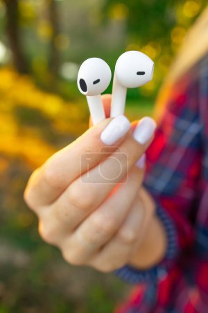 Photo for Female Fingers Holds Wireless Earbuds outdoors. Close-up view. - Royalty Free Image