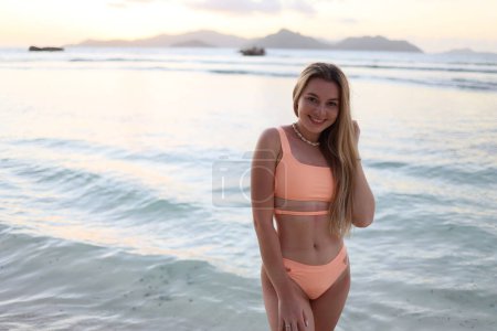 Photo for Of a beautiful woman with hangings on the seashore. Cheerful young woman smiling on the beach during summer vacation. Happy girl with blonde hair enjoying an evening walk - Royalty Free Image