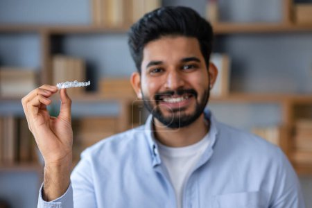 Téléchargez les photos : Jeune homme arabe avec barbe tenant un aligneur invisible orthodontique et des appareils dentaires regardant positif et heureux debout et souriant avec un sourire montrant des dents - en image libre de droit