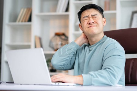 Photo for Millennial tired stressed man having a neck pain. Male touching massaging neck sitting at the desk working or studying indoors, suffering from discomfort long hours of sedentary overworking concept - Royalty Free Image