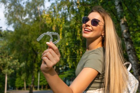 Téléchargez les photos : Femme gaie dans des lunettes de soleil tenant un aligneur de dents invisible tout en souriant - en image libre de droit