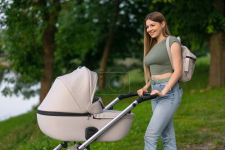 Téléchargez les photos : Concept de famille, d'enfant et de parentalité - mère heureuse avec poussette dans le parc près du lac. - en image libre de droit