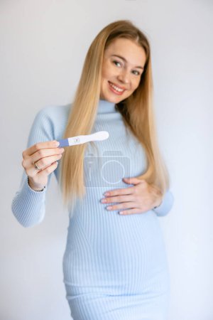 Foto de Hermosa mujer sosteniendo el resultado de la prueba de embarazo con un aspecto positivo y feliz de pie y sonriendo con una sonrisa perfecta - Imagen libre de derechos