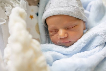 Photo for A sweet newborn baby boy is sleeping on her back in her crib, swaddled in a blue blanket. - Royalty Free Image