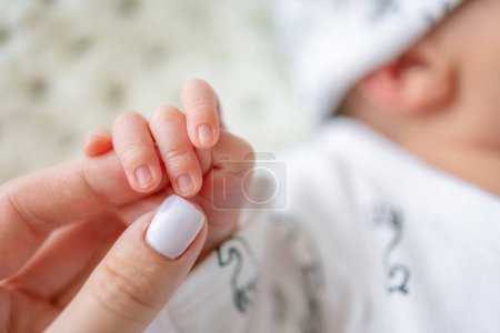 Téléchargez les photos : Gros plan petite main de bébé nouveau-né tenir doigt mère. L'enfant bébé a une prise ferme sur le doigt du parent après la naissance. Concept de famille et de maison. - en image libre de droit
