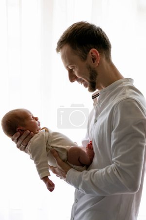 Foto de Feliz padre sosteniendo a un niño dormido en las manos. Padre abrazando a su pequeño hijo de un mes. Estilo de vida auténtico vida real conmovedor momento tierno. - Imagen libre de derechos