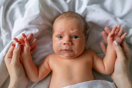 Foto de Un bebé recién nacido sorprendido yace sobre una manta blanca y sostiene el dedo de la madre. - Imagen libre de derechos